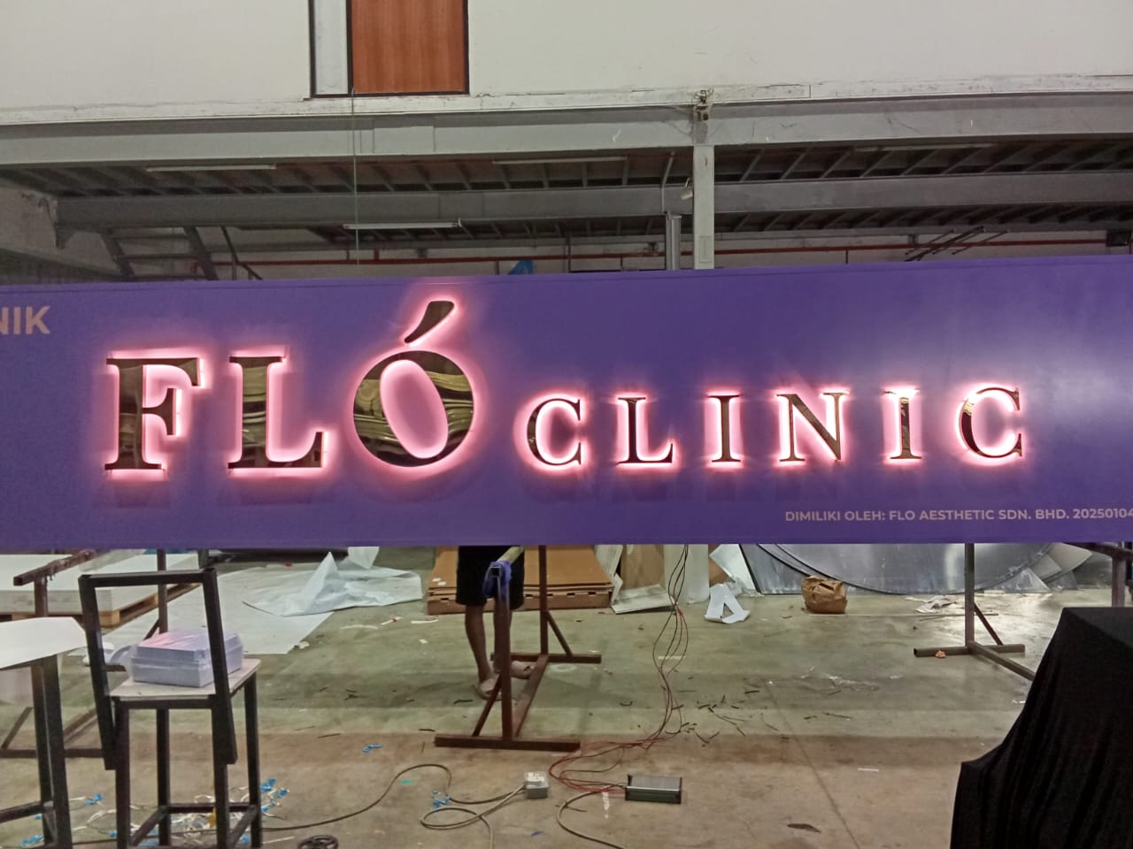 FLO Clinic backlit signboard with warm halo glow around dark lettering on a purple panel